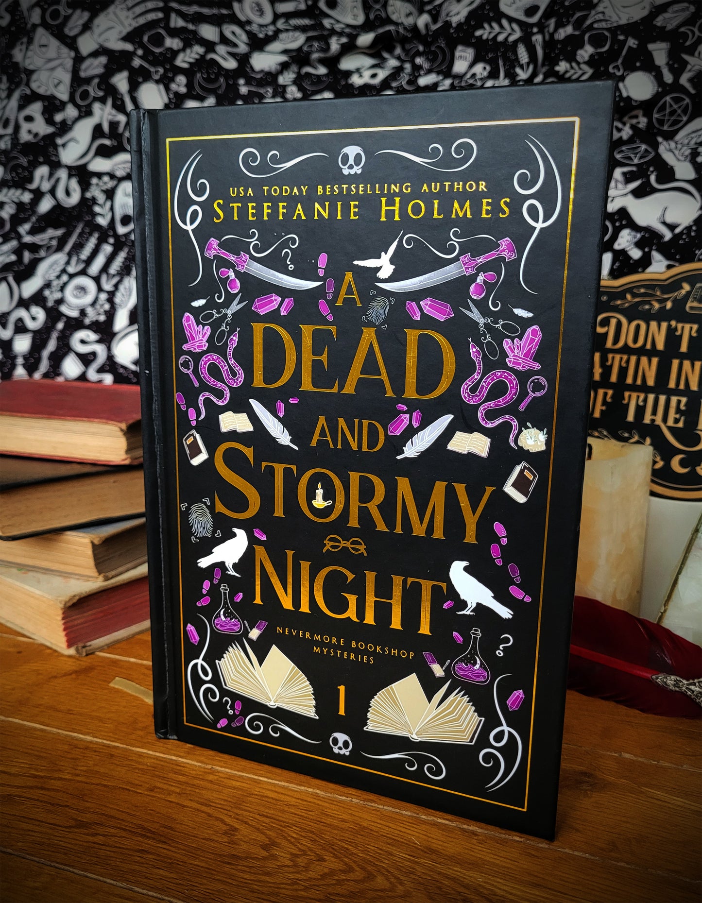 'A Dead and Stormy Night' luxe hardcover by Steffanie Holmes infront of a stack of books and patterned backdrop