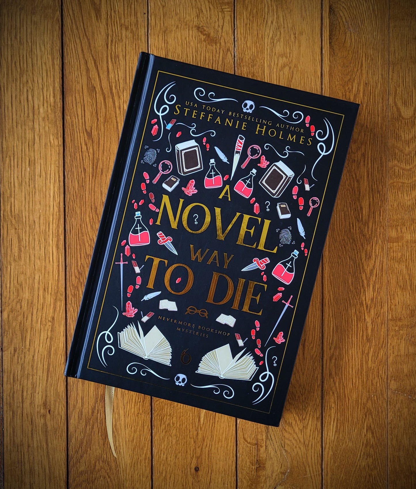 A hardcover edition of the book 'A Novel Way to Die' by Steffanie Holmes, featuring a black cover with red and gold decorative elements and text.
