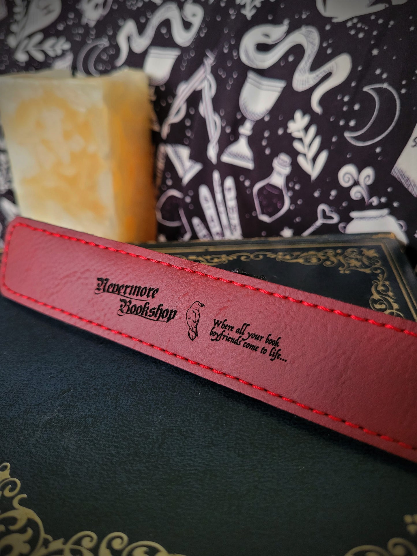 a red leatherette bookmark featuring the Nevermore Bookshop logo, a raven and 'WHERE ALL YOUR BOOK BOYFRIENDS COME TO LIFE' inscription