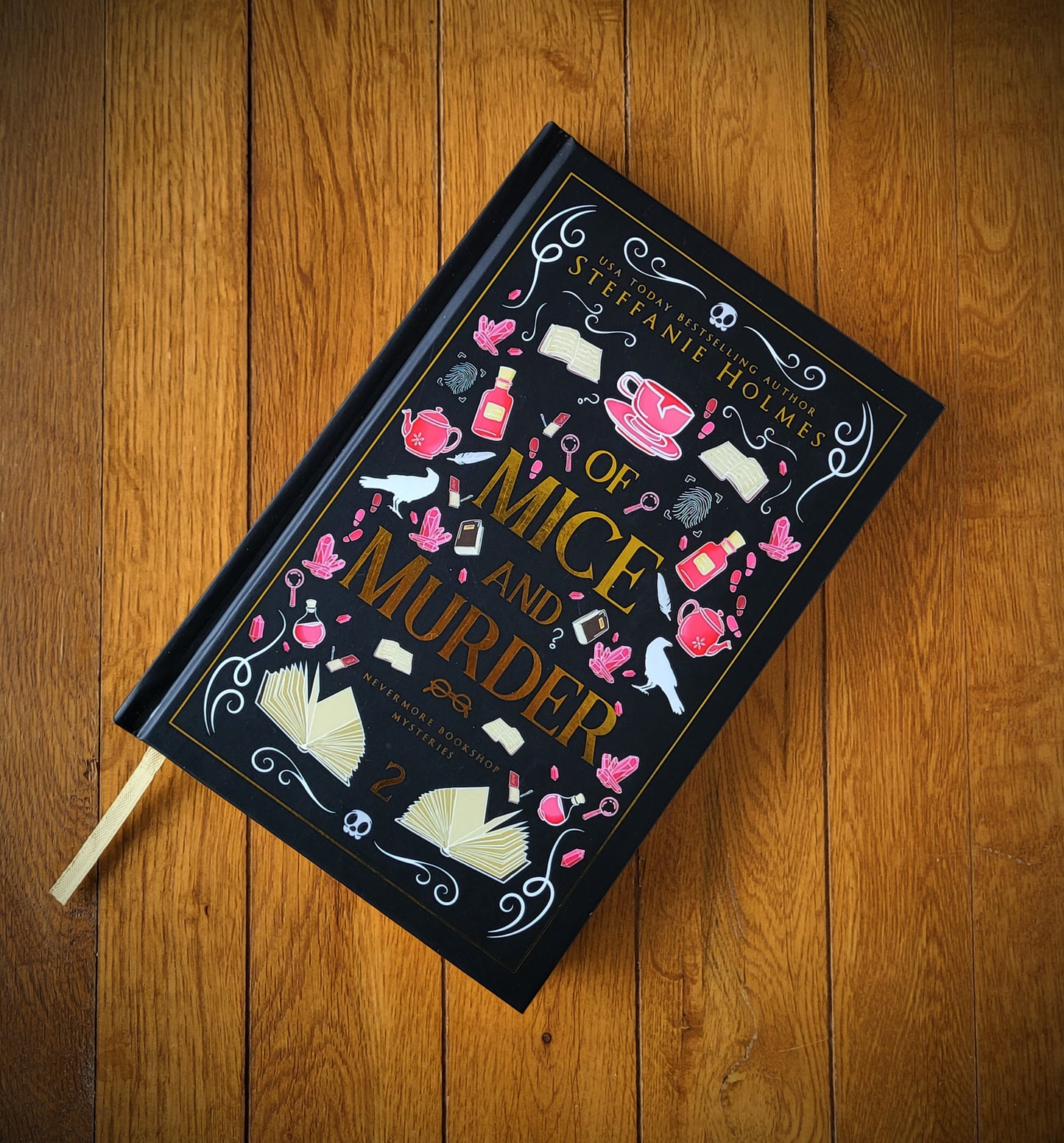 A hardcover edition of the book 'Of Mice and Murder' by Steffanie Holmes, featuring a black cover with pink and gold decorative elements and text.