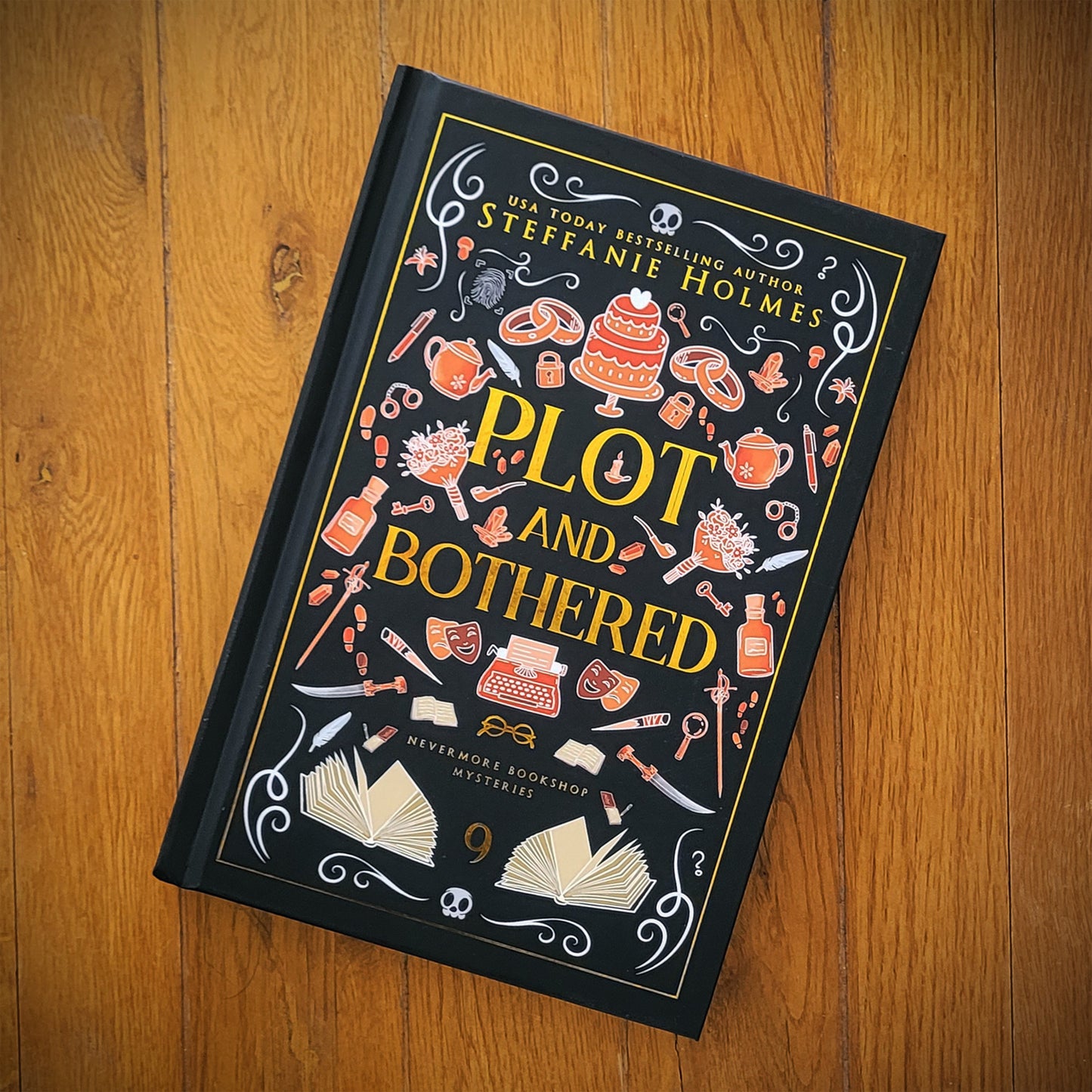 A hardcover edition of the book 'Plot and Bothered' by Steffanie Holmes, featuring a black cover with orange and gold decorative elements and text.
