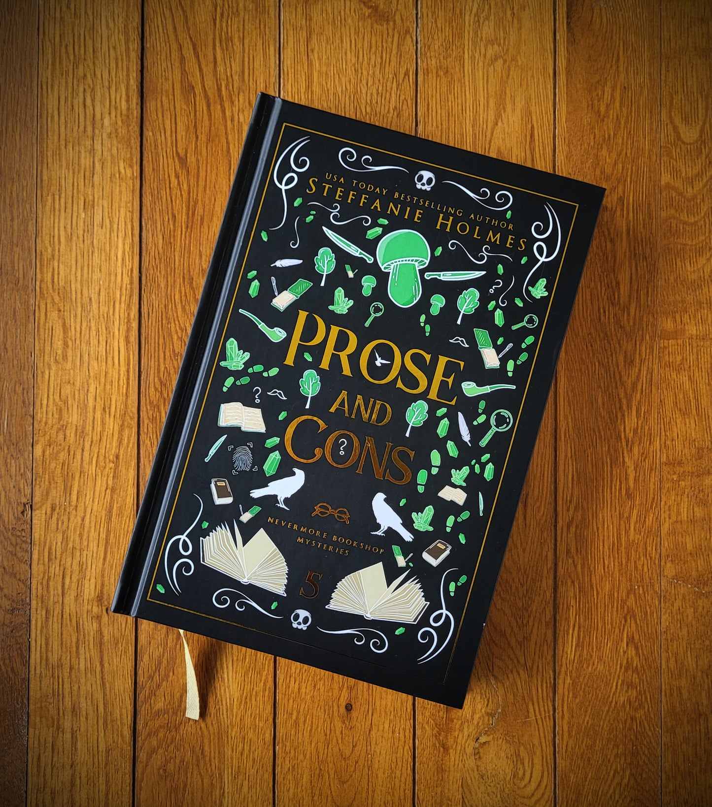 A hardcover edition of the book 'Prose and Cons' by Steffanie Holmes, featuring a black cover with green and gold decorative elements and text.
