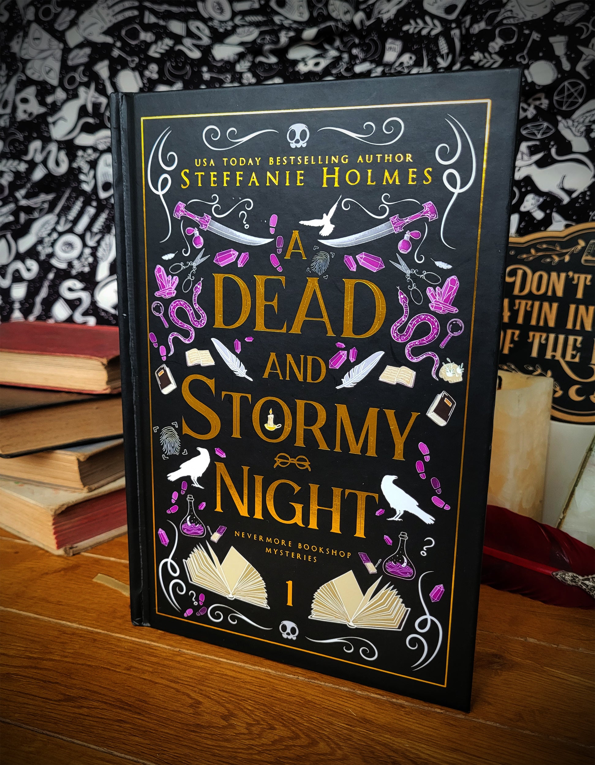'A Dead and Stormy Night' luxe hardcover by Steffanie Holmes infront of a stack of books and patterned backdrop