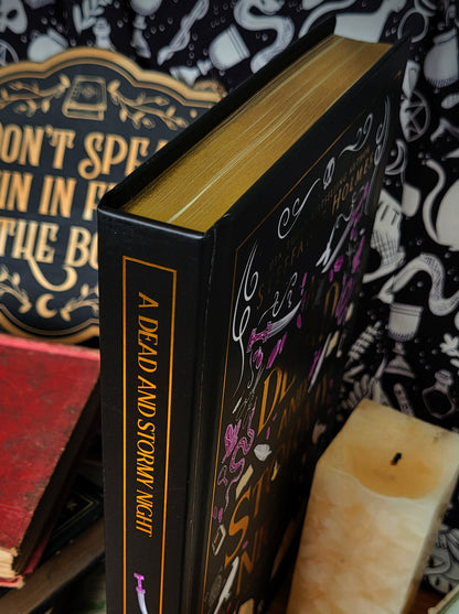 'A Dead and Stormy Night' luxe hardcover by Steffanie Holmes infront of a stack of books and patterned backdrop