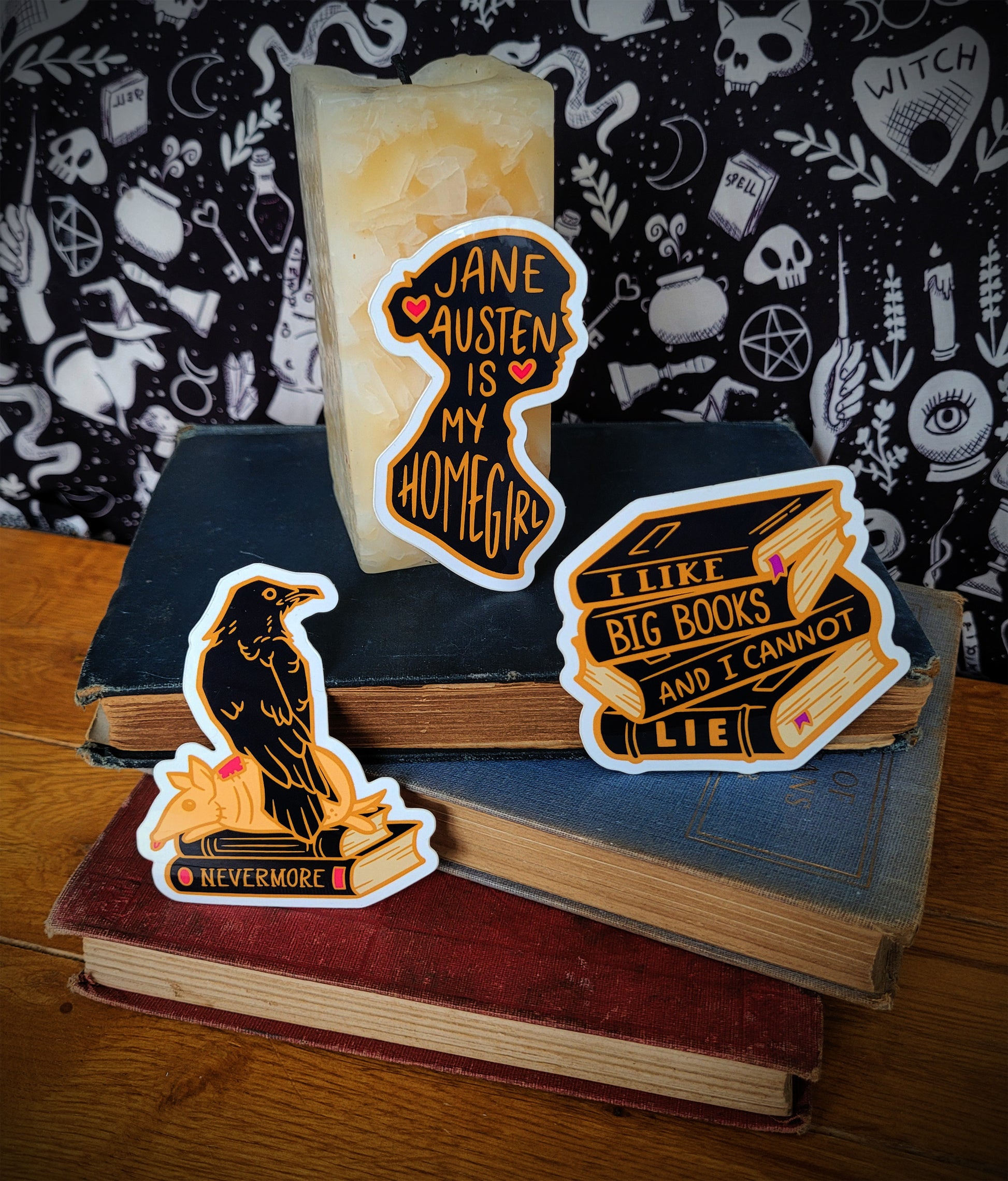 A set of Nevermore-themed vinyl stickers displayed on top of books, featuring various designs including a crow, a book with a quote, and other mystical elements.