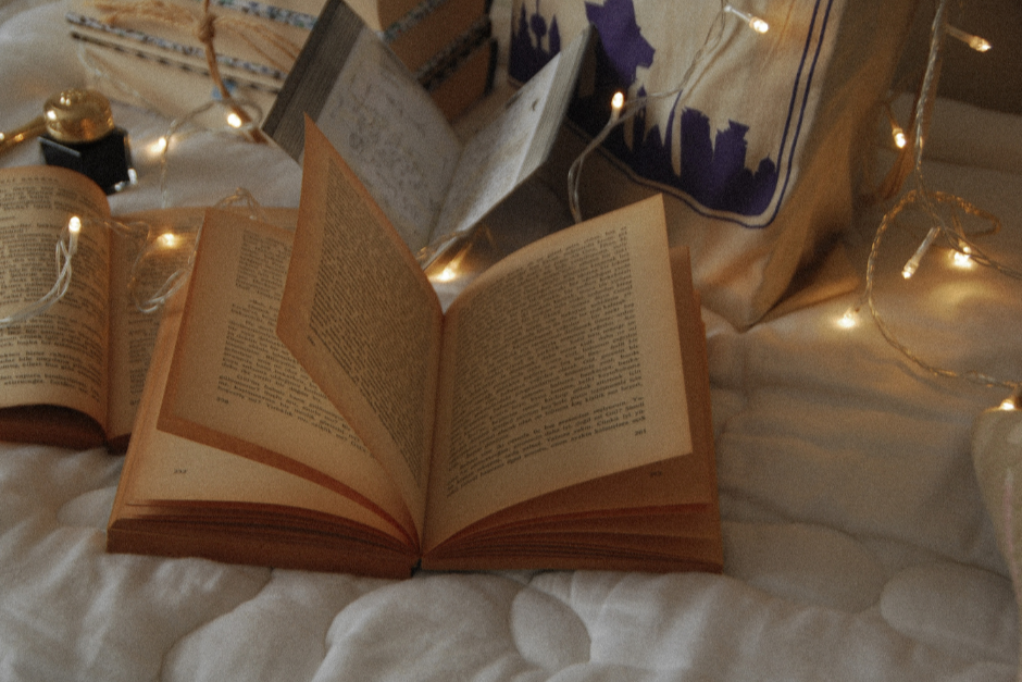 Open book on a surface with string lights and a pillow in the background
