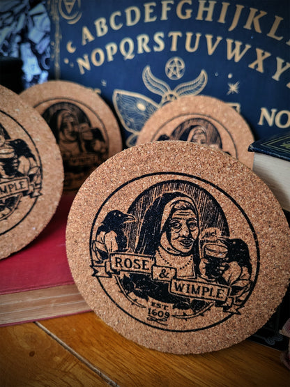 A set of round cork coasters with a black and beige Rose & Wimple design, displayed on a surface.