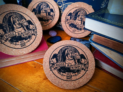 A set of round cork coasters with a black and beige Rose & Wimple design, displayed on a surface.